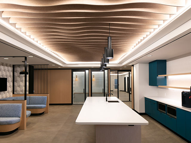 A sculptural wood-slat ceiling rises above 2 gray flannel banquettes, complete with video screens, in the entry of Work Better Coworking Offices in Tribeca