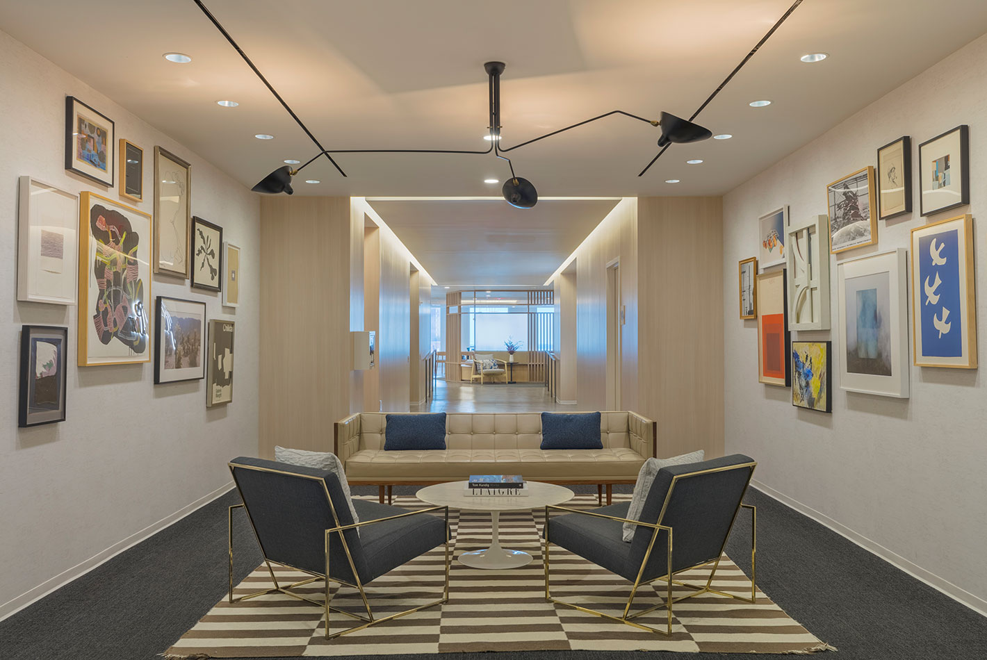 Artworks is hung gallery style on the walls of this casual conference room at J Crew Headquarters. A striped rug anchors a sofa and 2 angular club chairs.