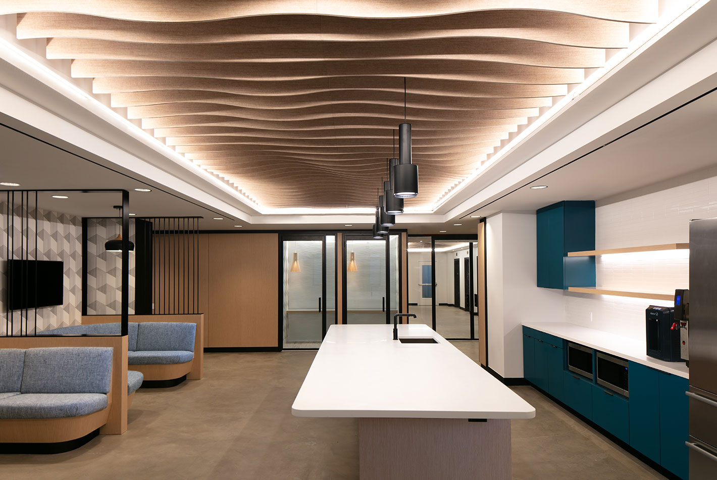 A sculptural wood-slat ceiling rises above 2 gray flannel banquettes, complete with video screens, in the entry of Work Better Coworking Offices in Tribeca