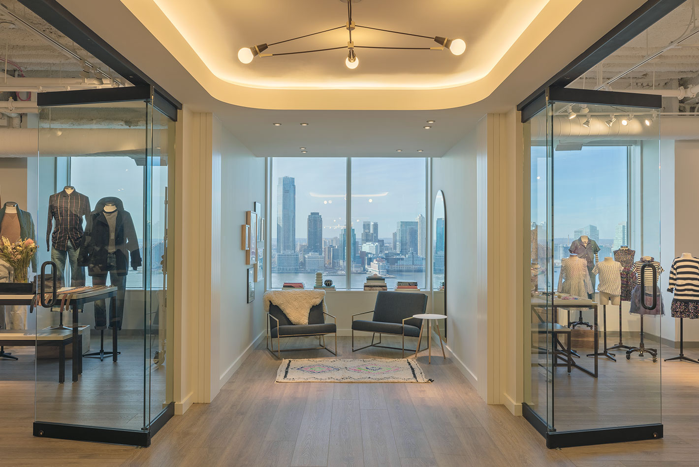 Plate glass walls showcase the Hudson river and the New Jersey skyline in the store vignette area at J Crew Headquarters. Club chairs provide a place to sit.