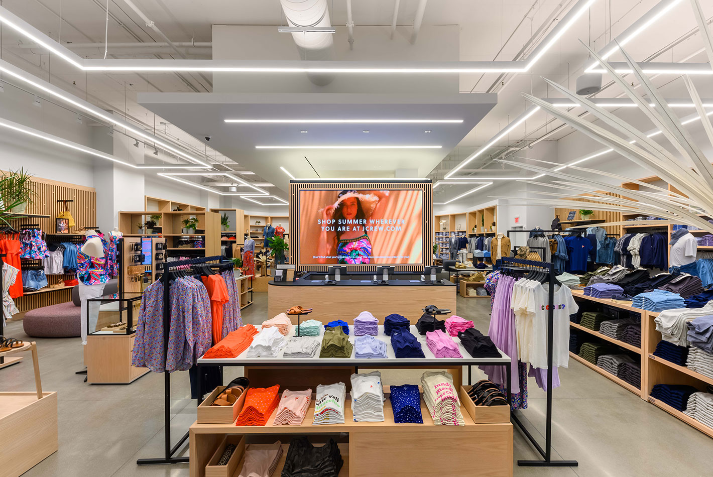 Innovative rectangular light fixtures hang from the ceiling at the cashier's desk of J Crew's newly designed store. New oak shelving holds the women's collection