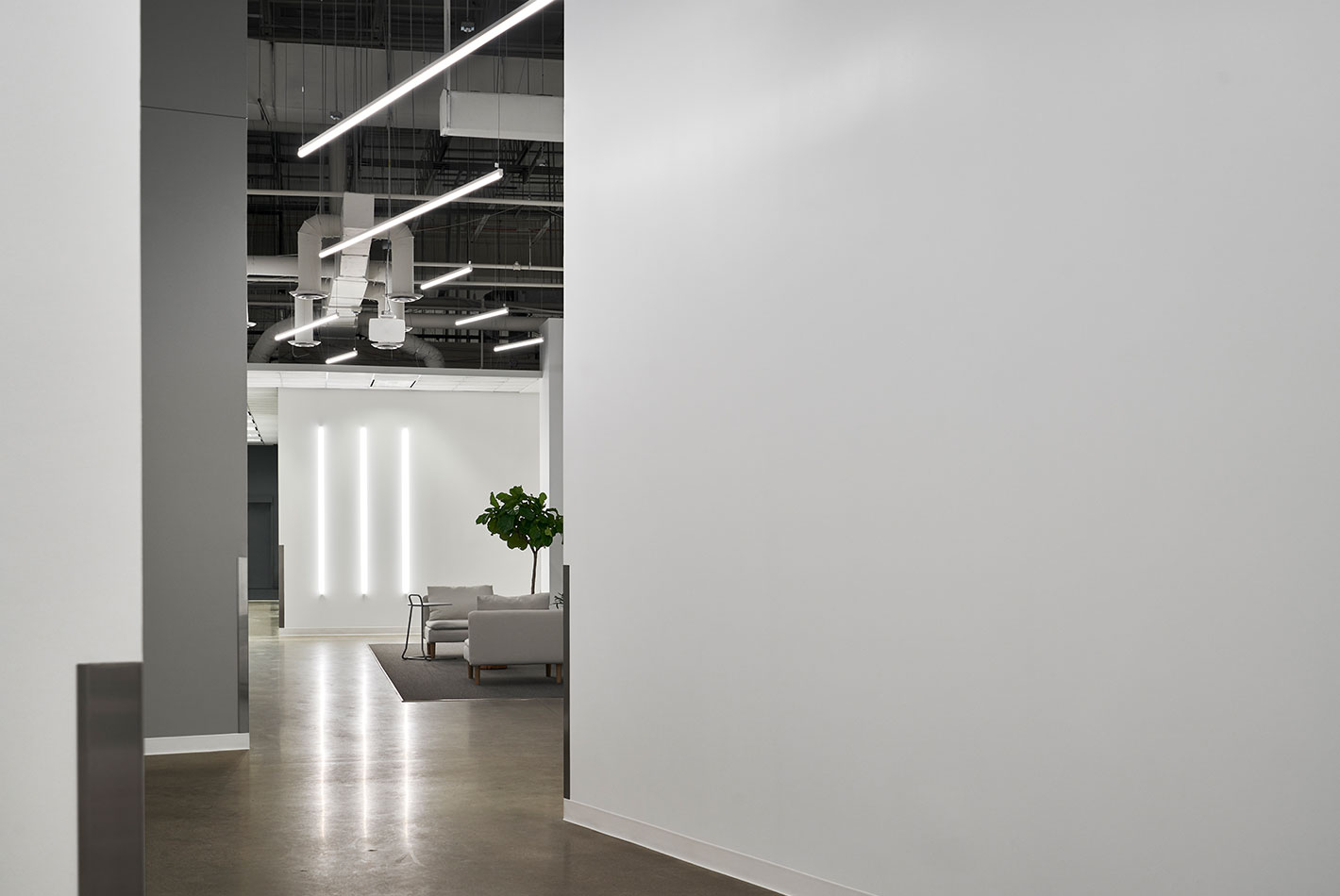 Polished concrete floors, industrial duct work, and gleaming white walls create a transitional hallway at Postmates headquarters.