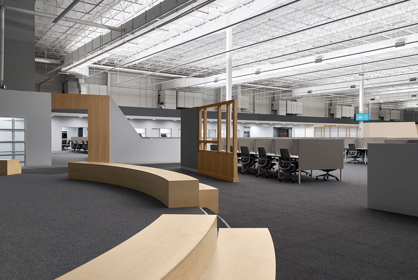 A curved and raised platform creates a stage at Postmates Headquarters. High, industrial ceilings with ample light are set against charcoal industrial carpet