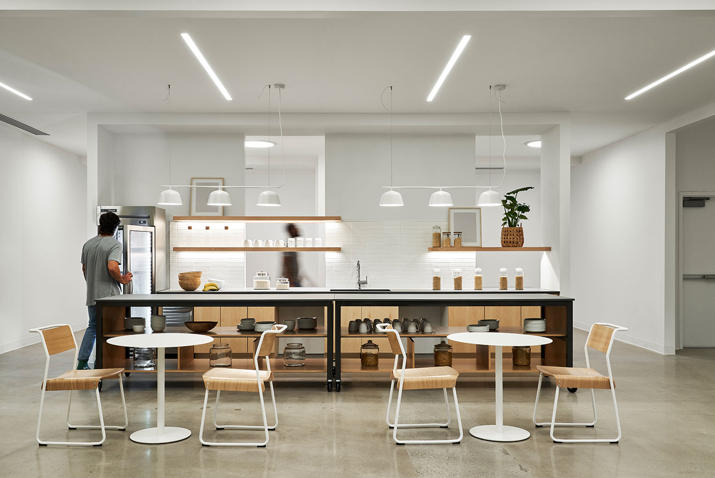 The employee cafe area at Postmates Headquarters features tables and chairs in front of a working service area, complete with refrigerator and sink.