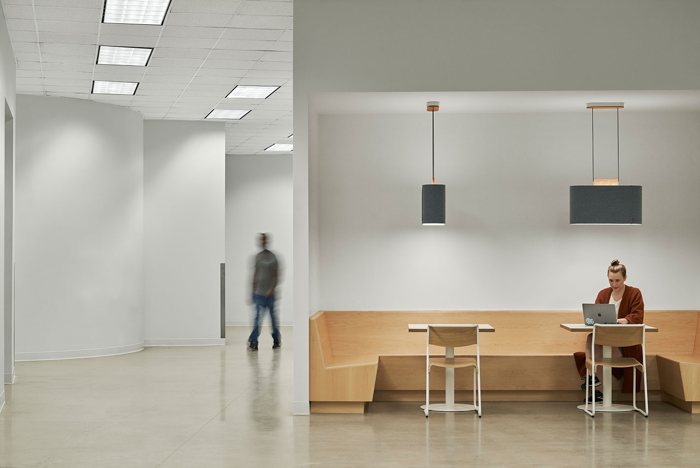 A wood-veneered corner banquette area in Postmates Headquarters. 2 overhead light fixtures illuminate the space.