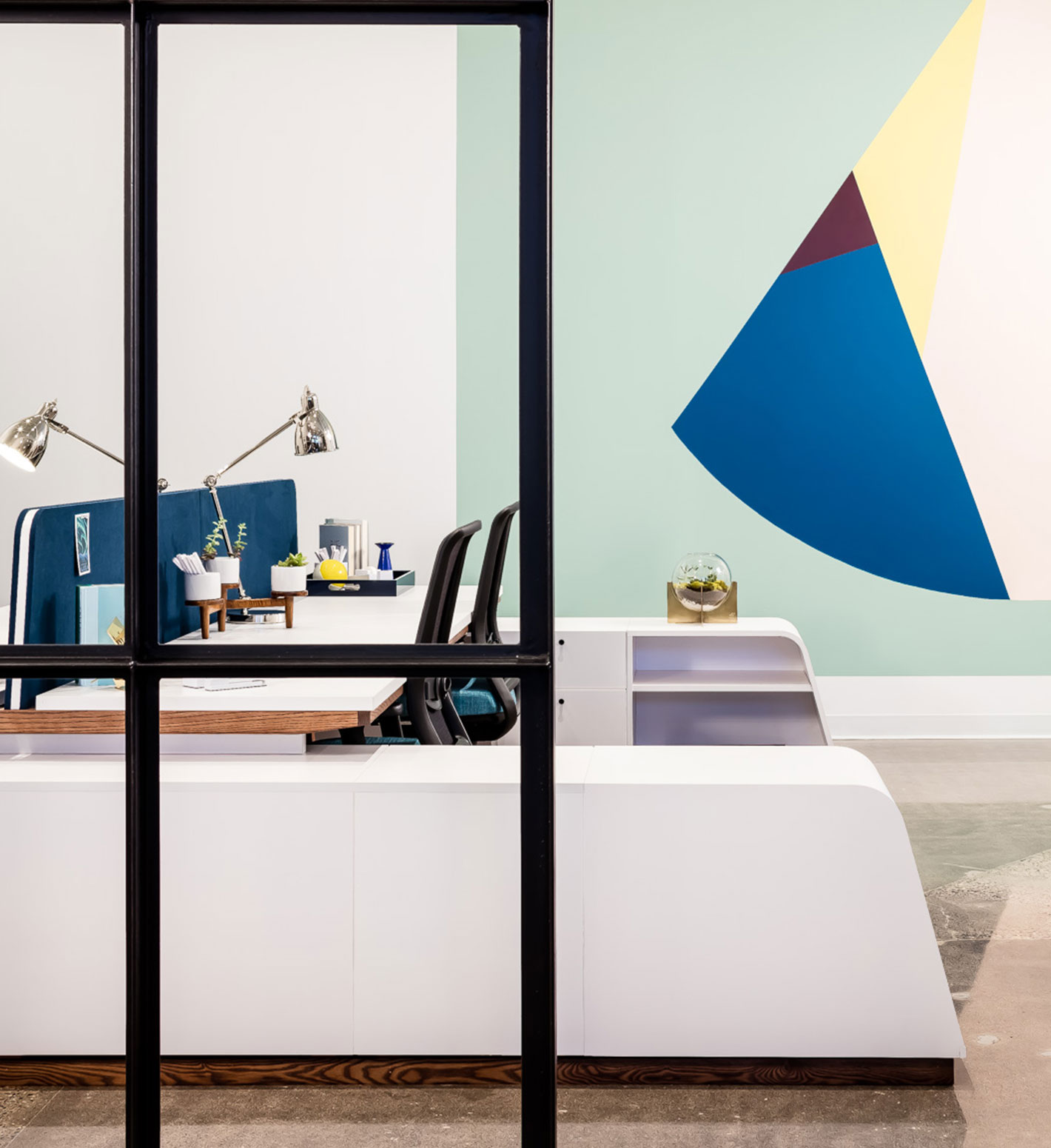 An abstract painting hangs on the wall near a desk area featuring angular white cabinets.