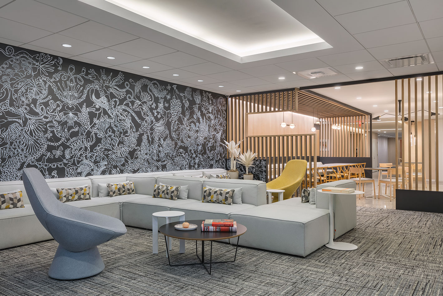 Highly stylized wallpaper and mid-century patterned carpeting create a playful atmosphere in the lounge area of J Crew Headquarters. Long intersecting sectional furniture provides seating