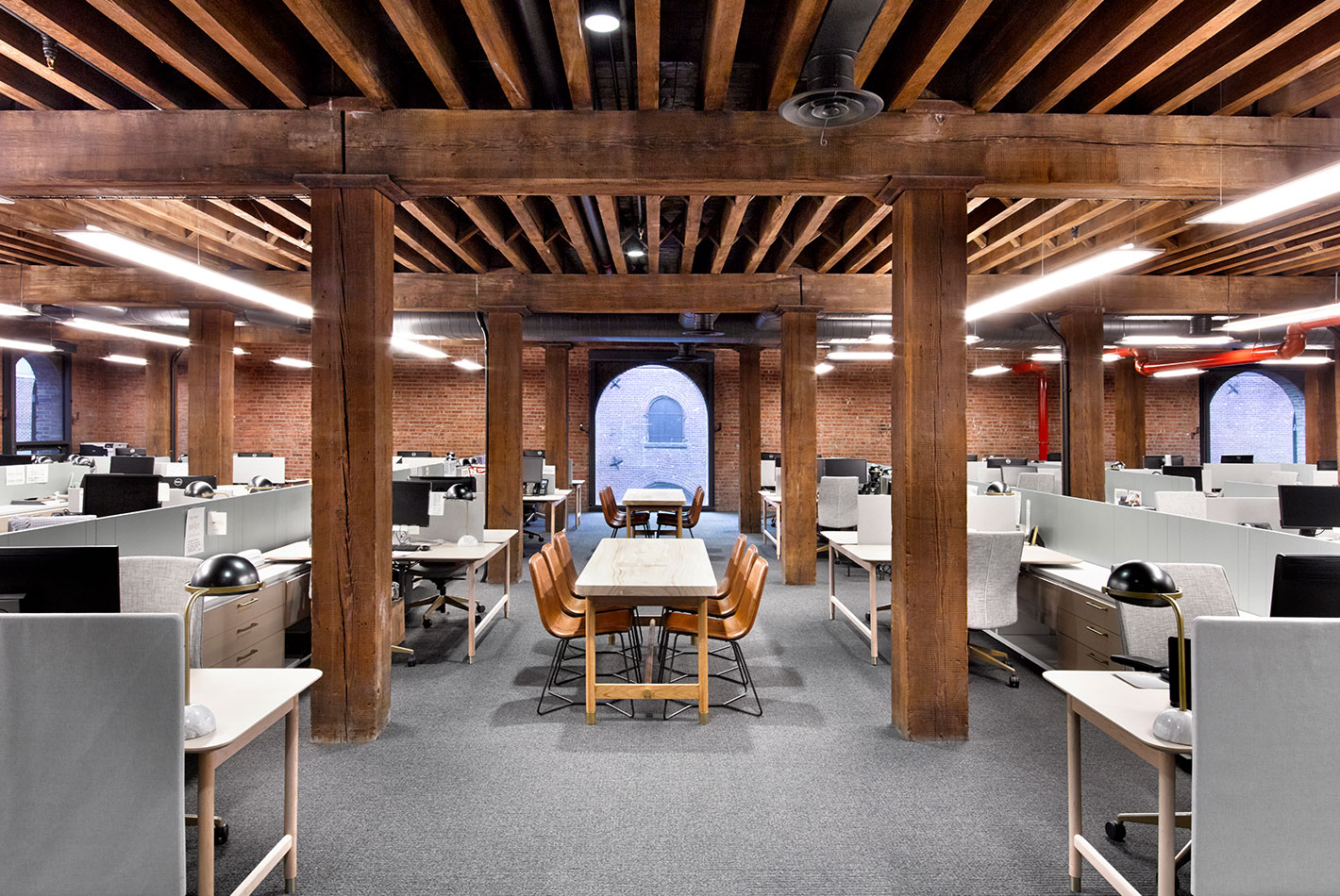 Original 19th century wood columns and ceiling beams contrast with light office furniture in the offices at West Elm Headquarters. An arched window is at the back of the space.