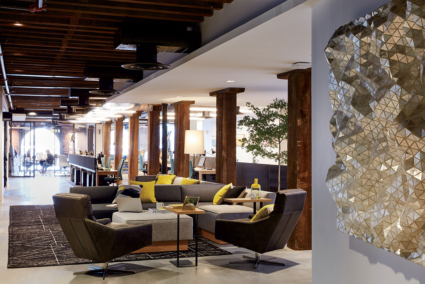 A wall sculpture of cascading pyramids welcomes visitors in an area designed for casual meeting at West Elm Headquarters. Low leather club chairs and wood tables populate the area.