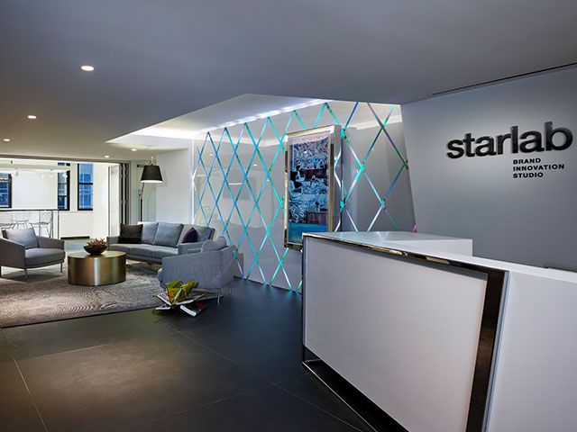 The lobby of Starwood Design Studio features upholstered seating and a brightly lite diamond-patterned wall