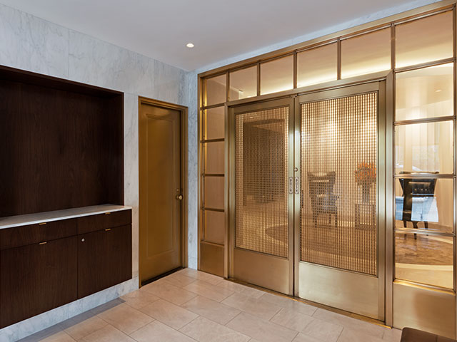 A walnut desk in the lobby of 1056 5th Avenue, which has a marble floor and walls. Satin brass doors complete the design