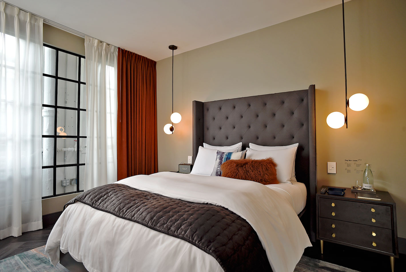 A grey queen-sized sleigh-bed in a West Elm Hotel model room with terra cotta colored curtains.