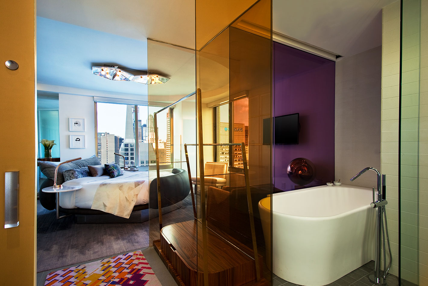Brightly colored glass panels separate the bathroom and bedroom at W Hotel's Presidential Suite. A full circular bed faces full city-view windows.