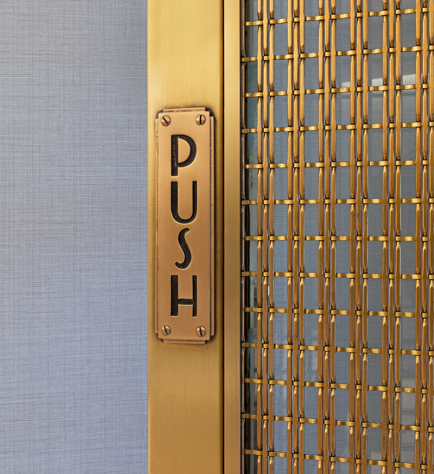 A detail image of a satin brass door with the word PUSH on it.