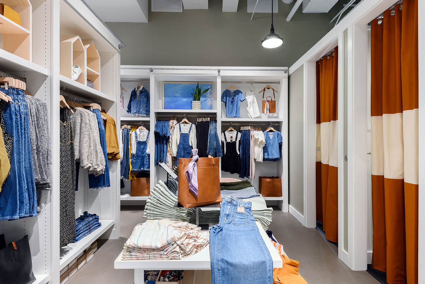 The women's department at Madewell features a collection of indigo-hued clothing and accessories. Dressing rooms nearby are covered in canvas panels.