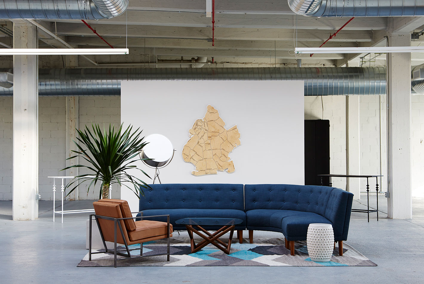 A curved blue sofa and brown club chair are anchored by a geometric carpet at West Elm's Maker's Studio